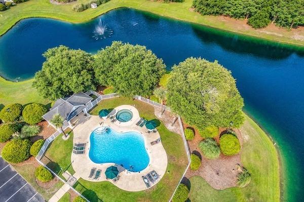 Aerial view of an outdoor pool and hot tub beside a pond with a fountain in Pawleys Island, South Carolina.